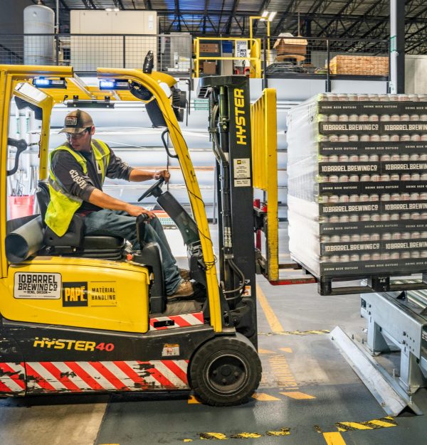 A warehouse worker maneuvers a forklift to transport crates for brewing company storage.